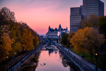 Fall foliage around the Rideau Canal, with the exterior of the landmark hotel Fairmont Chateau Laurier and pink sunset sky. Autumn view of downtown Ottawa, Ontario, Canada, November 2021. - obrazy, fototapety, plakaty