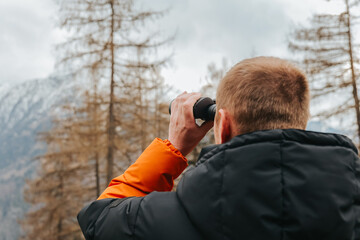 Viewing the mountains with binoculars.Hiking in the mountains in the spring season.Man with binoculars. man in a warm jacket looks through binoculars at a mountain landscape. walking in the mountains