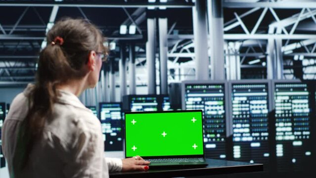 Qualified worker in server farm housing high end rows capable of quickly and efficiently performing complex computations and data analysis, using mockup laptop to get rid of problems