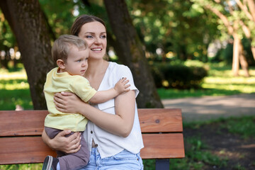 Fototapeta premium Happy nanny with cute little boy on bench in park, space for text