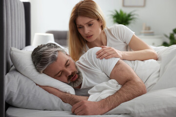 Irritated woman waking up her snoring husband in bed at home