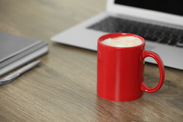 Red ceramic mug with hot drink on wooden table desk at workplace. Mockup for design