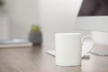 White ceramic mug and computer on wooden table at workplace. Space for text