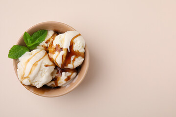 Scoops of ice cream with caramel sauce and mint leaves on beige table, top view. Space for text