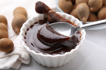 Taking tasty tamarind sauce with spoon from bowl on white table, closeup