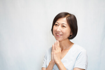 Fototapeta premium 上を向いて笑顔で手を合わせる中年女性