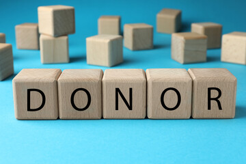 Wooden cubes with word Donor on light blue background