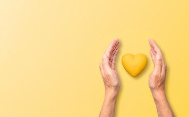 Hands enveloping a heart in a protective manner against a bright yellow background, ideal for...
