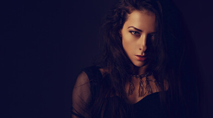 Fototapeta premium Beautiful woman in black dress posing in fashion necklace on the neck. Long hairstyle on dark shadow background. Toned vintage color banner portrait. Closeup.