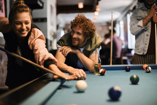 Young and diverse group of friends playing pool together in a bar
