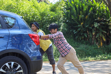 Men pushing a broken car down the road