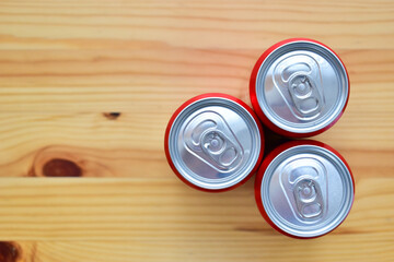 three aluminium red cans of soft drink put on brown wooden table