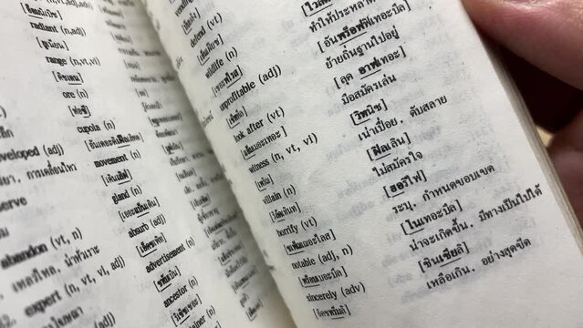 Hand open Thai - English dictionary for reading. Close-up macro shot looking through a book turning the pages. Business and education concept 