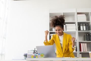 African American businessman gets good news, celebrates success with arm up in front of laptop at desk, happy excited African American woman celebrates victory sitting in coworking 