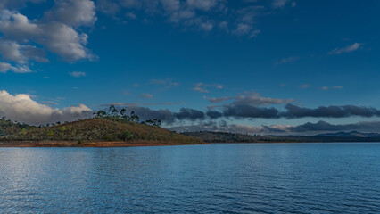 Beautiful blue lake. Coastal hills with green vegetation against the sky and clouds. Ripples on calm water.  Madagascar. Mantasoa Lake.