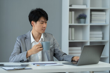 Young Asian businessman sitting at work holding a cup of coffee during the break Relax after working for a long time in calculating, analyzing, researching financial reports. startup business ideas