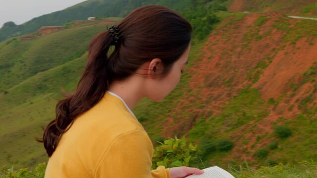 slow camera orbit around a woman reading on a hillside with her hair blowing in the wind