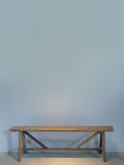 An empty blue grey color wall with a wooden bench against the wall, spotted lighting from above, empty space for copy or text insert, graphic resource