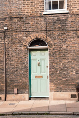 Puerta color verde agua con detalles dorados sobre pared de ladrillo y ventana arriba en Londres