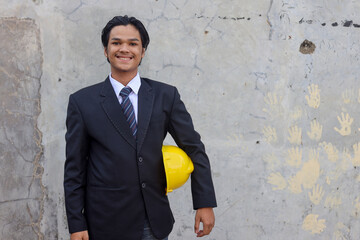 Confident young Asian engineer or businessman wearing black suit holding yellow helmet