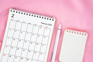 The February 2024 month calendar and pen with open diary on pink fabric background. Monthly...