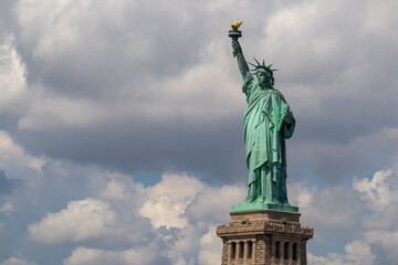 Obraz premium Iconic representation of freedom and independence, the Statue of Liberty with flaming torch on Liberty Island. The Lady on a Pedestal is surrounded by clouds. City landmark. American history.