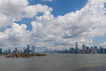 Captivating New York and New Jersey urban skyline with striking and modern skyscrapers reflecting on water seen from The Liberty Island. Think clouds above the city. Modern city.