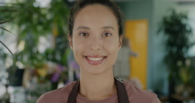 Portrait of positive Middle Eastern woman with beautiful smile standing in flower shop wearing uniform. Retail and successful business concept.