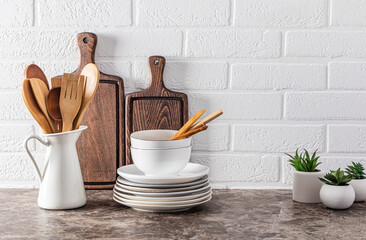 Fototapeta na wymiar Stylish kitchen background with a set of white utensils and wooden kitchen utensils on a marble dark countertop against a white brick wall.