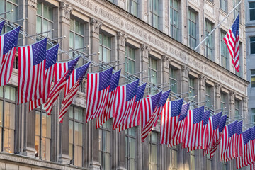 A row of American flags attached to a building in New York City. The flags are gently waving on the wind. The building in the back looks very traditional. Financial quarter.