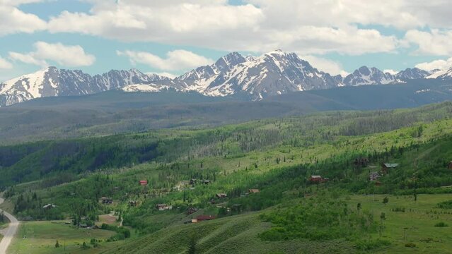 Closeup aerial view of beautiful Colorado mountain range with snow capped peaks on a sunny, blue sky day in the summer with green fields, trees, and mountain homes