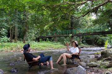 Happy couple sitting on a wooden chair surrounded by greenery chatting happily on weekends. Talk happily in the middle of the stream.