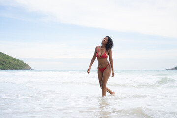 Fototapeta na wymiar Portrait of happy young woman in red bikini walking on the beach.