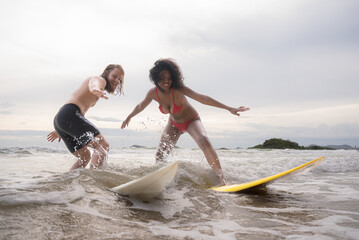 Couple surfing on the beach having fun and balancing on the surfboard