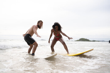 Fototapeta na wymiar Couple surfing on the beach having fun and balancing on the surfboard