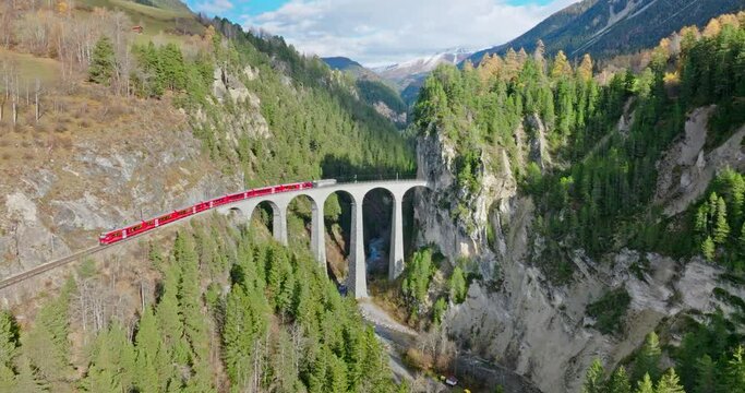 Landwasser Viaduct world heritage sight with luxury Glacier and Bernina express in Swiss Alps summer autumn scenery. Aerial Drone shot red train passing through famous mountain in Filisur, Switzerland