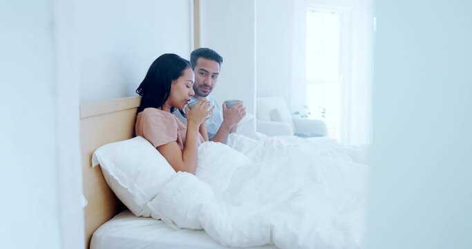 Love, morning and a couple drinking tea in bed together while in their home to relax on a weekend. Coffee, smile or happy with a man and woman talking in the bedroom of their apartment for romance