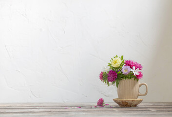beautiful flowers in cup on wooden table on background white wall