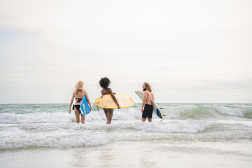 Two women and young man holding surfboards ready to walk into the sea to surf.