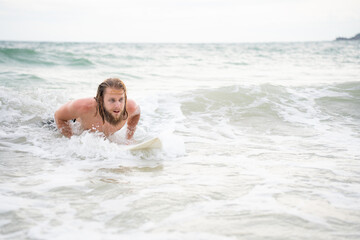 Young man surfing on the beach having fun and balancing on the surfboard
