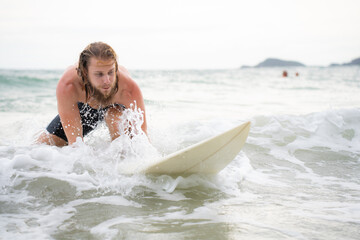 Young man surfing on the beach having fun and balancing on the surfboard