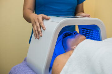 Latin woman cosmetologist makes Led phototherapy for the face.