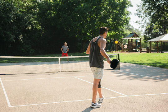 Two young adults playing a game of pickleball near a playground