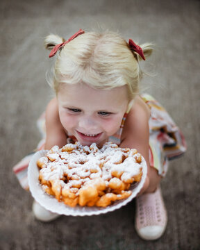 Excited little girl holding a funnel cake at county fair