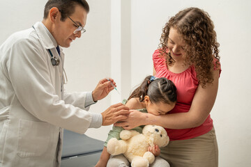 hispanic girl crying while being injected by a pediatrician. Latin doctor injecting a child with a...