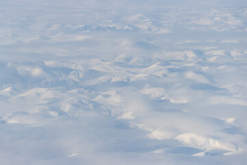 Aerial view of snow-capped mountains and clouds. Winter snowy mountain landscape. Icheghem Range, Kolyma Mountains. Koryak Okrug (Koryakia), Kamchatka Krai, Siberia, Far East Russia. Great background.