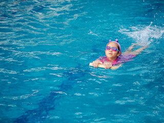 Asian child or kid girl wearing swimming suit to learning on swimming pool , learn and training swim on kick board
