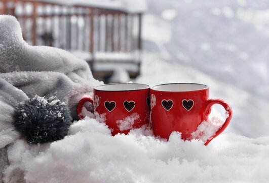 two red mugs with heart shaped on the snow and blanket