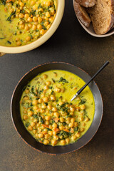 Healthy tasty lunch, soup with chickpeas and spinach, with spices and fresh herbs, with coconut milk on a brown background, top view