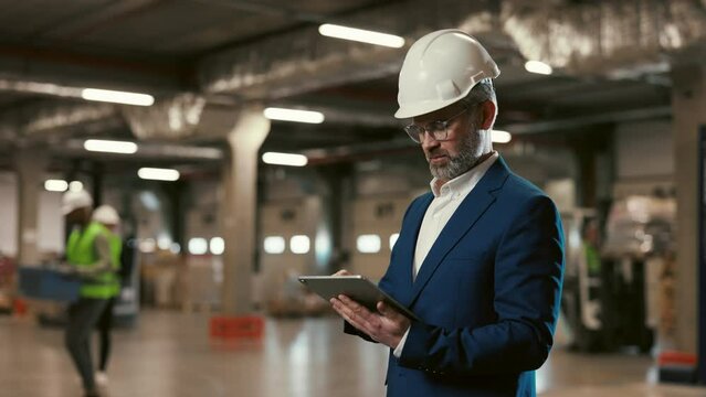 Portrait of Mature Worker Checks Products Stock and Inventory with Digital Tablet Standing in Storage. Male Manager Using Device While Working in Depository. Logistic and Technology Concept